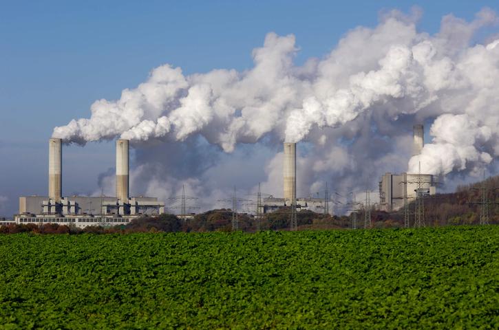 Imagem mostra uma indústria emitindo grande quantidade de fumaça no céu, provavelmente um processo de emissão de gases de efeito estufa.