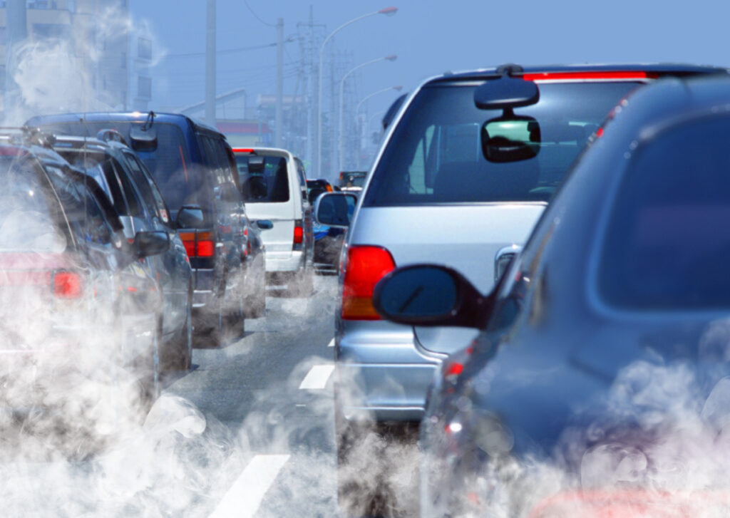 : Imagem mostra uma fila de carros no trânsito produzindo uma quantidade alta de fumaça branca, resultando na poluição do ar e destacando a importância da descarbonização