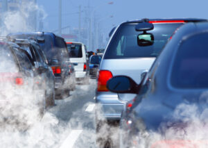 : Imagem mostra uma fila de carros no trânsito produzindo uma quantidade alta de fumaça branca, resultando na poluição do ar e destacando a importância da descarbonização